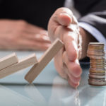 Human Hand Stopping Wooden Blocks From Falling On Stacked Coins